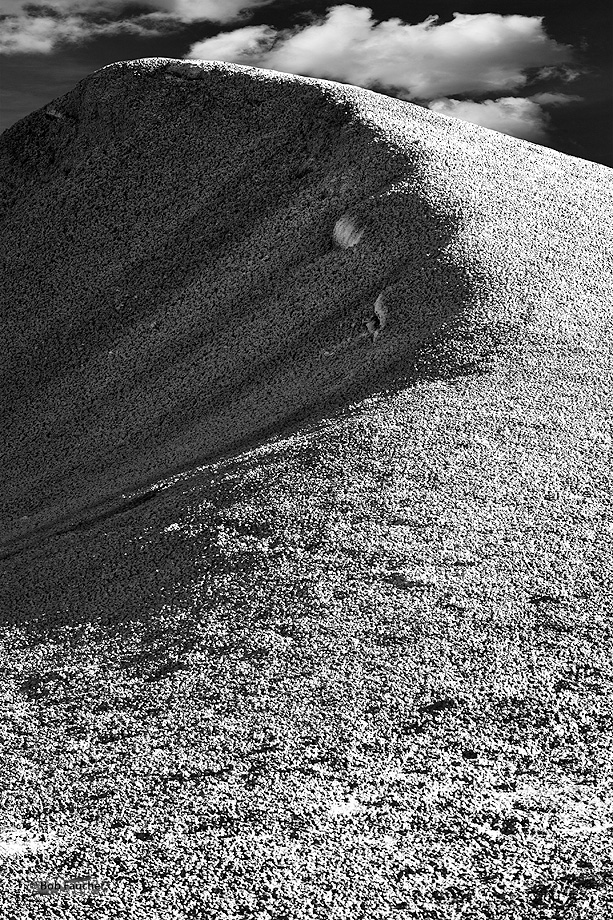 Bentonite mound with pronounced erosion on one side appears like a cresting wave or wind-driven sand dune