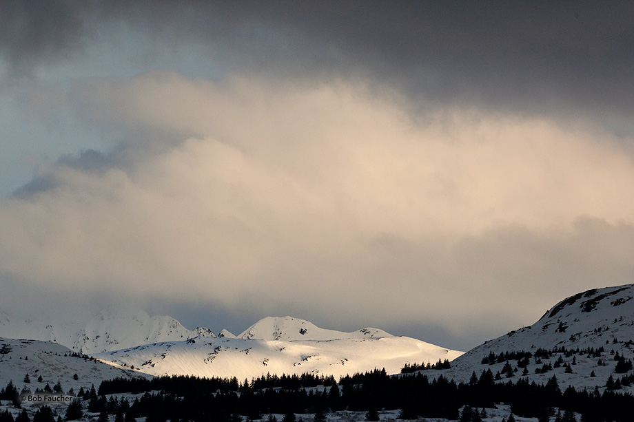The lower flanks of Barometer Mountain, as seen from Buskin Lake, are illuminated by the sun breaking below a late afternoon...