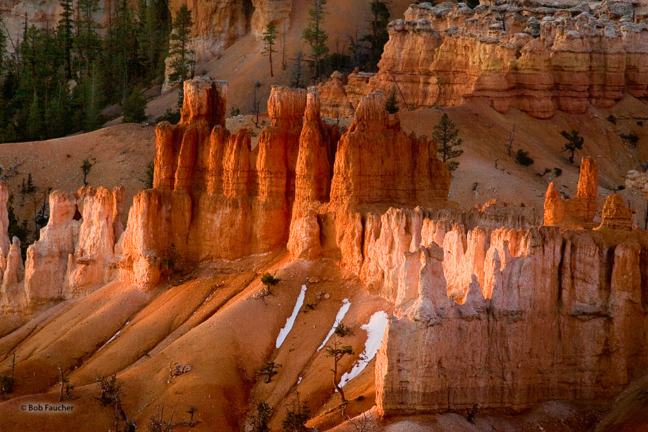 Early morning light makes the red hoodoos glow like fire while snow patches remain at their bases.