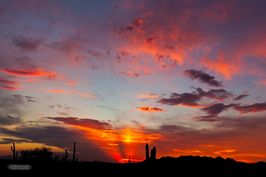 Low-hanging clouds are lit up by the sun's streaming rays breaking through the distant clouds on the horizon.