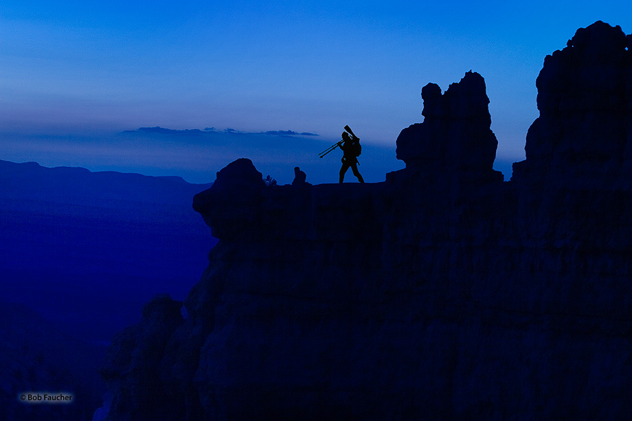 A photographer positions himself on a ledge overlooking Bryce Canyon in the early "Blue Hour" of morning to be able to capture...