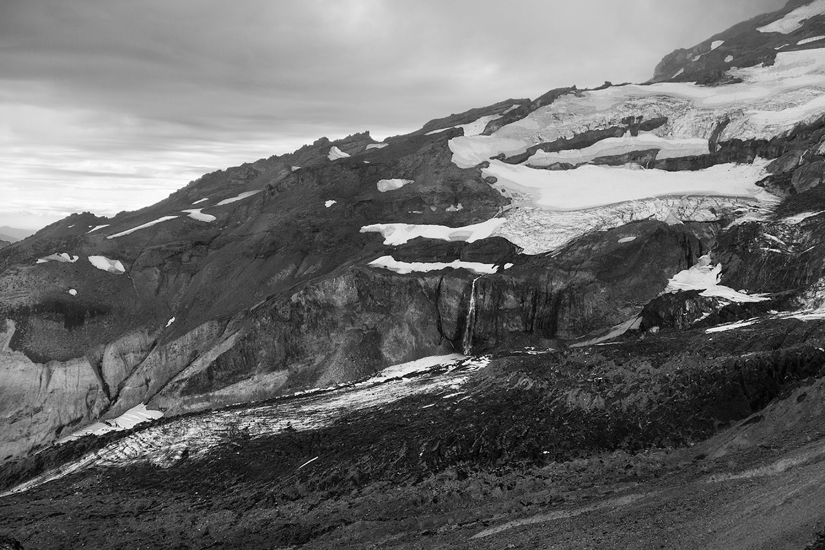 Small waterfall plummets over a cliff on the side of Mt. Rainier below a field of small glaciers