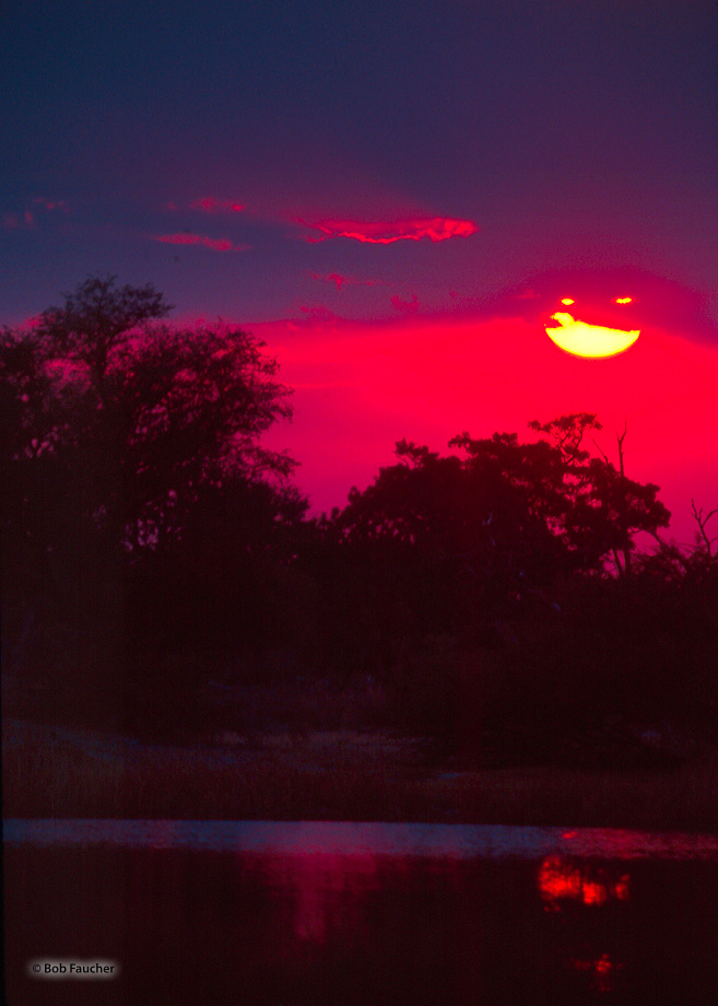 A break in the clouds over the Okavango Delta allow the setting sun and blazing red sky to peek through and slightly Illuminate...