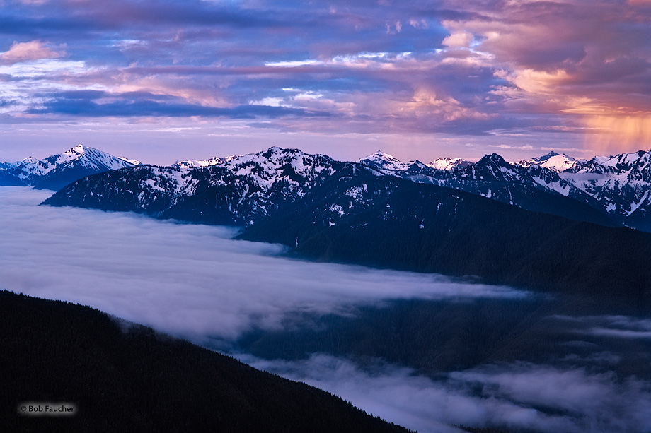 Dawn sunlight catches the tops of the Olympic range and highlights a squall while ground fog lingers in the Elwha Valley below...