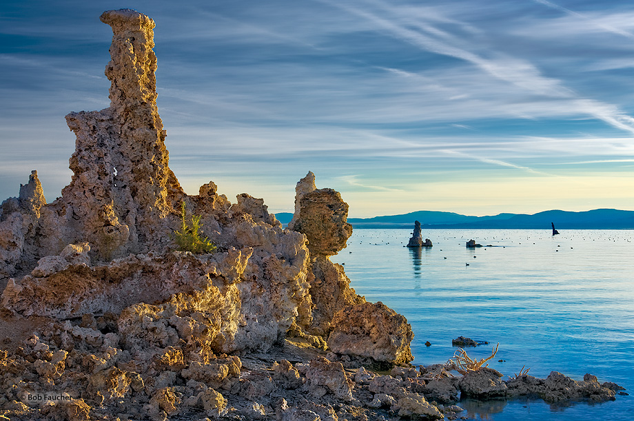 At sunrise a tufa tower is accenuated with direct, soft morning light while the sky and water reflect the warm light yielding...