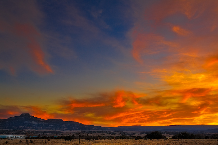 Skies blaze with late evening light on the clouds above Abiquiu Reservoir with Cerro Pedernal jutting above the horizon.