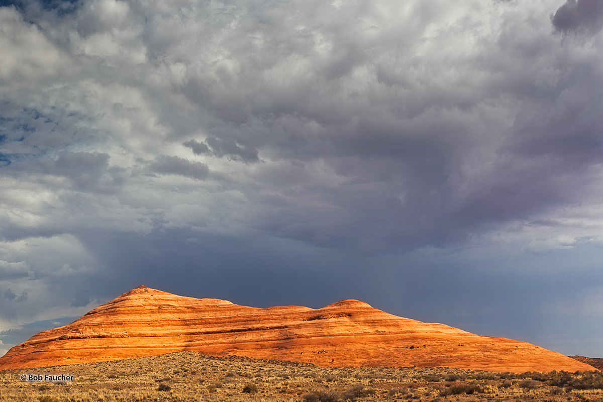 Beautifully stratified, erosion-rounded sandstone formation glows in morning light against dark foreboding skies in the Pedestal...