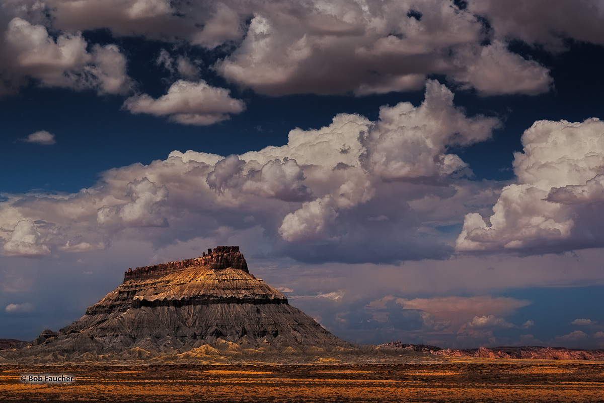 Late afternoon warm light breaks through heavy clouds to highlight the form and textures of Factory Butte, an isolated, flat-...