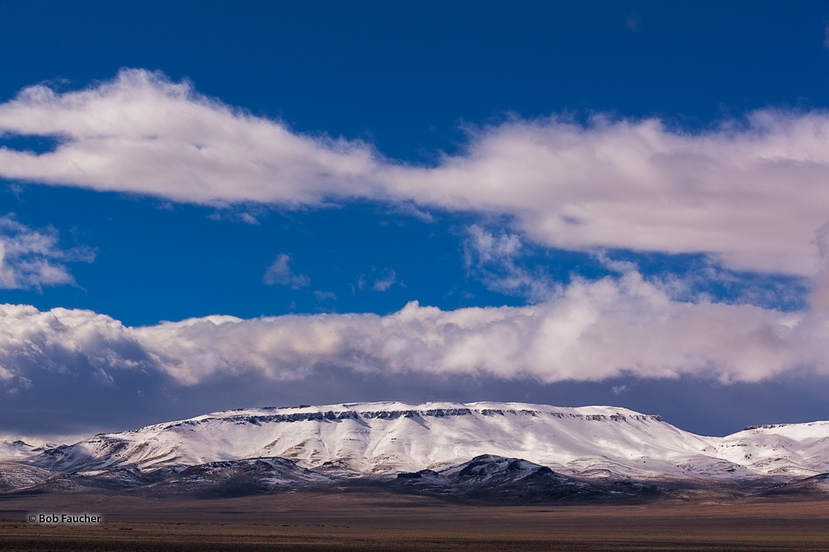 Snow covered bluff outside Fort McDermitt, NV. The flattened summit, layer of rock protruding through the snow below it and the...
