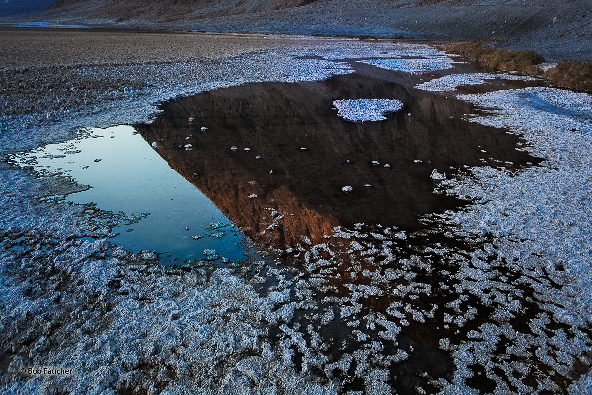 Afternoon light on the flanks of the Black Mountains is reflected in a pool in Bad Water Basin, Death Valley NP