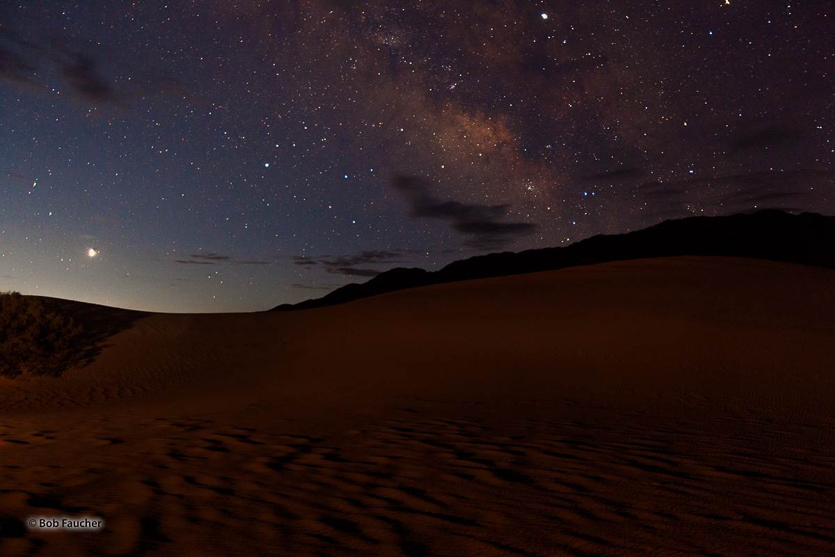 The Milky Way is poised over a section of the Mesquite Flat Sand Dunes. Artificial light with a red gel filter was painted onto...