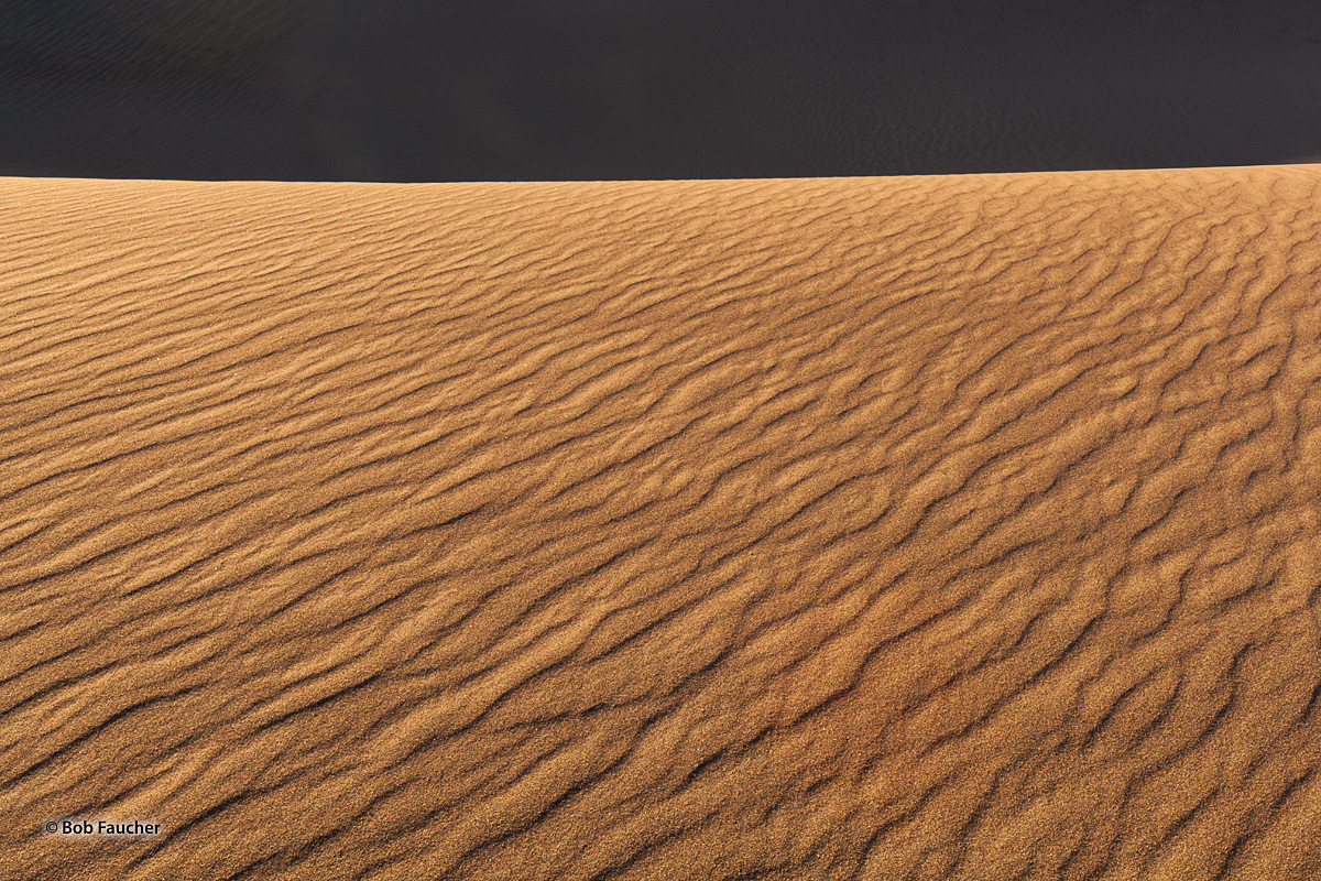 Morning light illuminates the east-facing surface of a sand dune while the dunes behind it remain in shadow, with only the slightest...