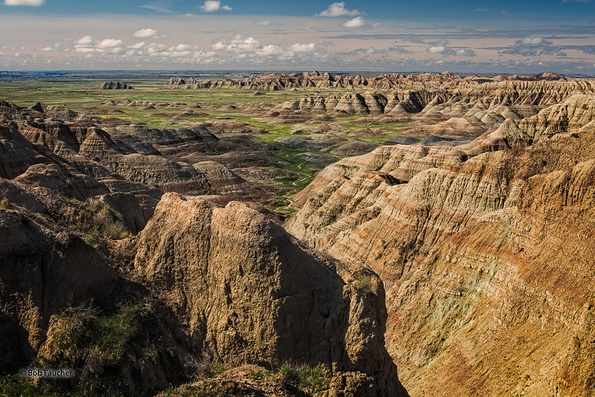 Colorful, eroded, striated formations lead into the grassy plain of  Burns Basin