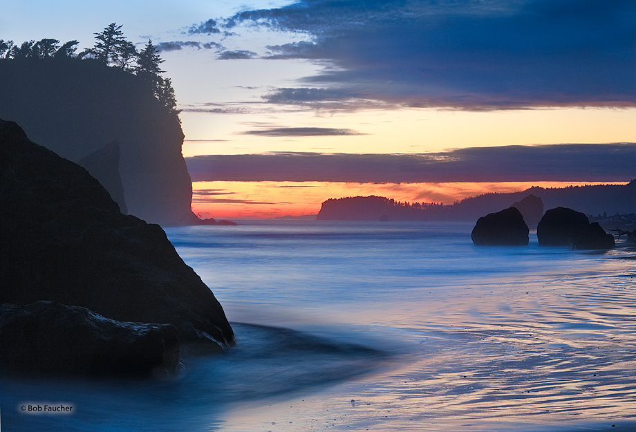 A long exposure flattens the surf as twilight glows below layers of clouds hanging above the beach punctuated with sea stacks...