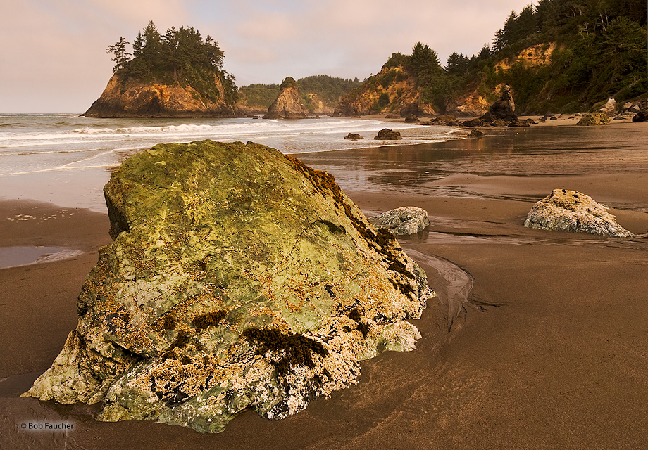 Soft, warm morning light on the vacant beach with clouds reflecting the light while Grandmother Rock (right background) looks...